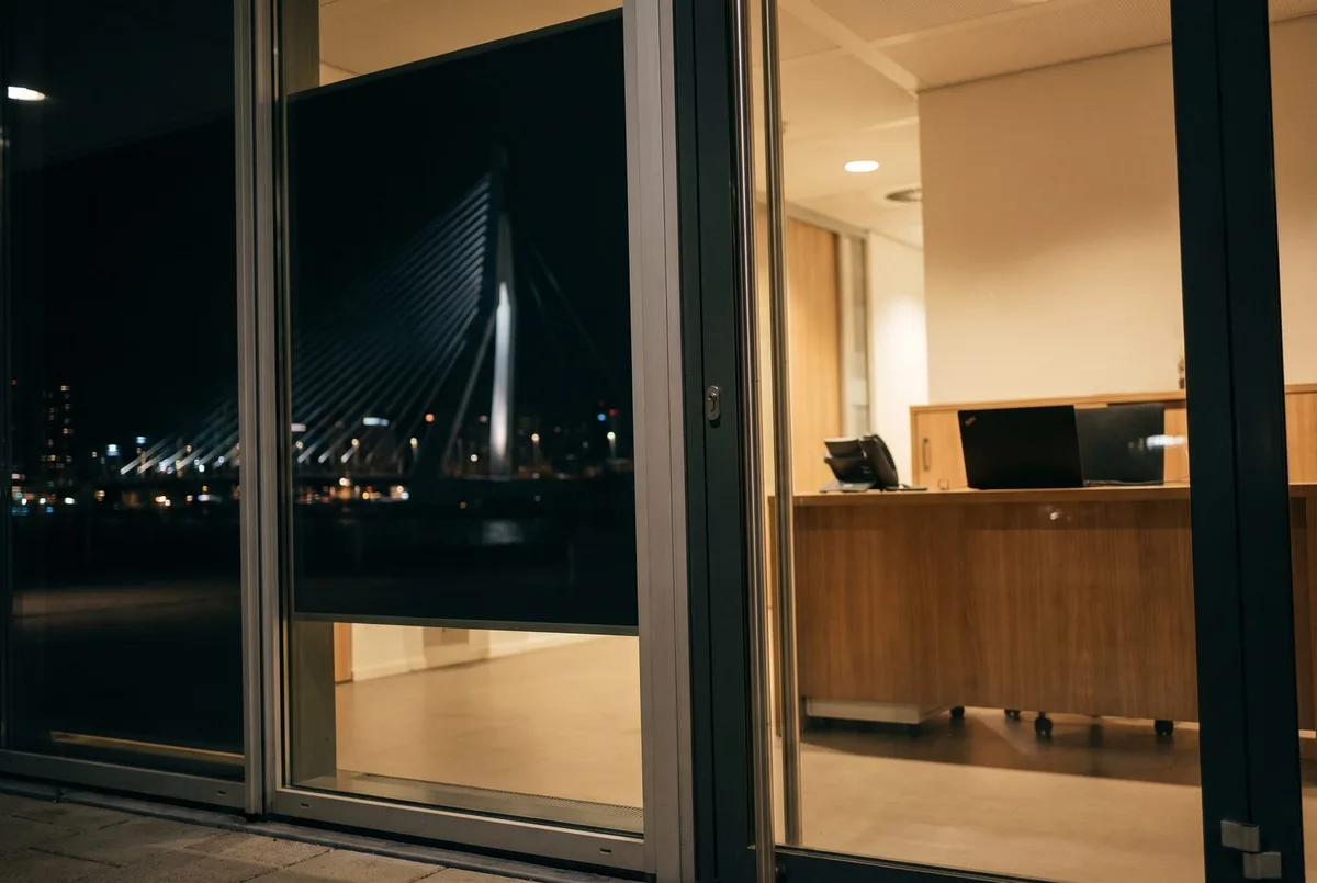 Kantooringang van Aanloop AI in Rotterdam in het blauwe uur, Erasmusbrug in het glas — neem contact op met onze AI-experts