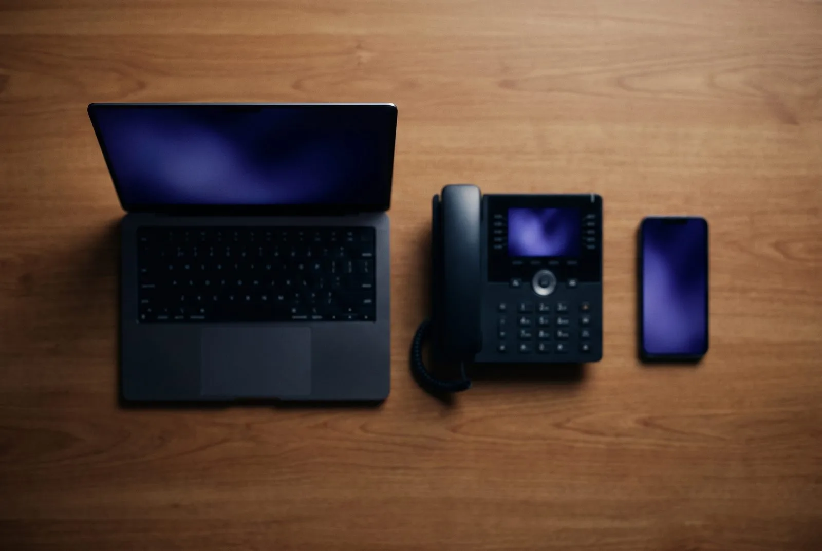 Laptop, bureautelefoon en smartphone op een rij, elk met een zachte AI-gloed — overzicht van 15 AI-oplossingen voor Nederlandse MKB